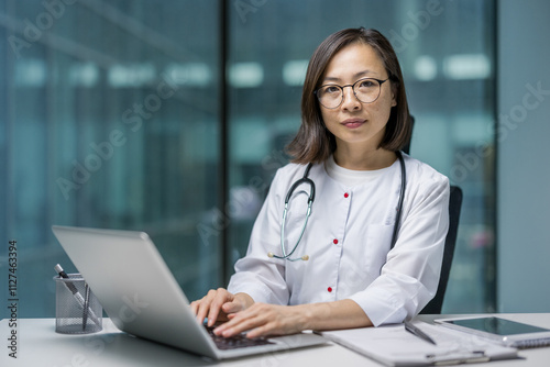 Quadro su tela Asian female doctor is focused on her work using a laptop in a contemporary office , showcasing professionalism and dedication in healthcare