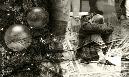 A Christmas tree with bright ornaments stands next to a person sitting on the ground with a small cup for coins, showing the contrast between holiday joy and poverty