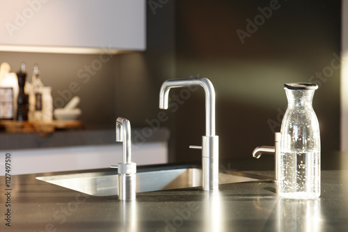 Modern kitchen countertop with stainless steel faucet, water dispenser, and glass pitcher.  Sleek design, dark granite surface.