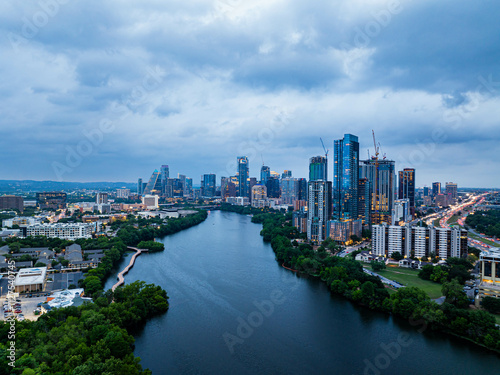 Aerial view of Austin, Texas skyline at dusk, showcasing modern skyscrapers reflecting on the Colorado River under a dramatic cloudy sky