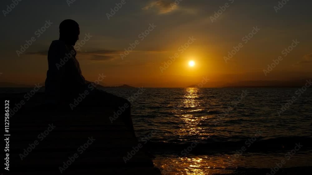Man feel lonely on pier. A silhouette of man feeling sorrow because of his loneliness on the wooden pier by the evening sea. Man feel lonely on pier. A silhouette of man feeling sorrow because of his loneliness on the wooden pier by the evening sea.