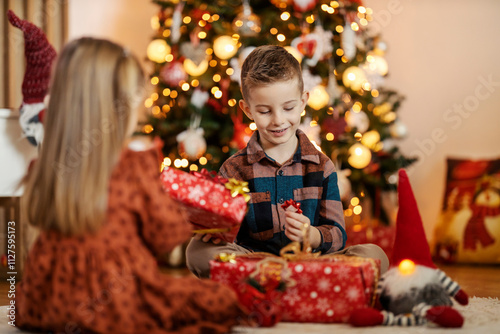 Loving adorable siblings sitting at warm home on christmas eve and exchanging gifts.