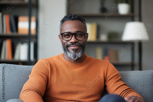 Smiling man in orange sweater sitting on gray couch