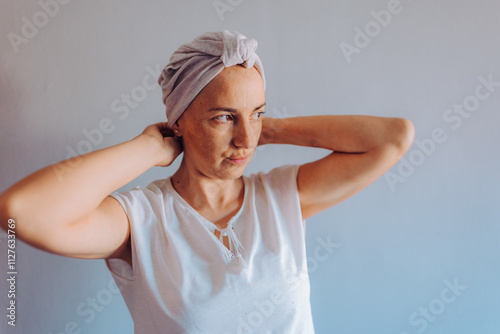 A woman with cancer delicately adjusts her headscarf, radiating confidence and self-care, depicting a moment of personal grooming and self-expression in a serene setting. photo