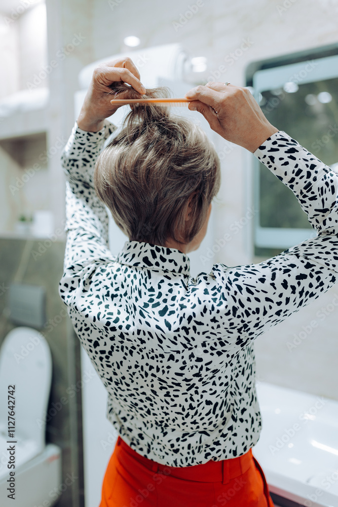 Naklejka premium A close-up shot focuses on a woman's hands combing her hair in a bright bathroom, highlighting the importance of personal grooming and daily beauty rituals.