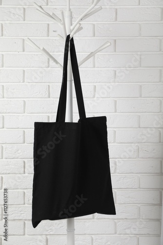 Black eco bag hanging on clothing rack near white brick wall. Mockup for design photo