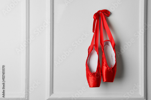 Foto Pair of beautiful red pointe shoes hanging on white wall, space for text