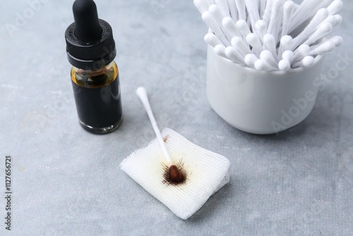 Bottle of iodine with dropper, piece of bandage and cotton swabs on grey table, closeup