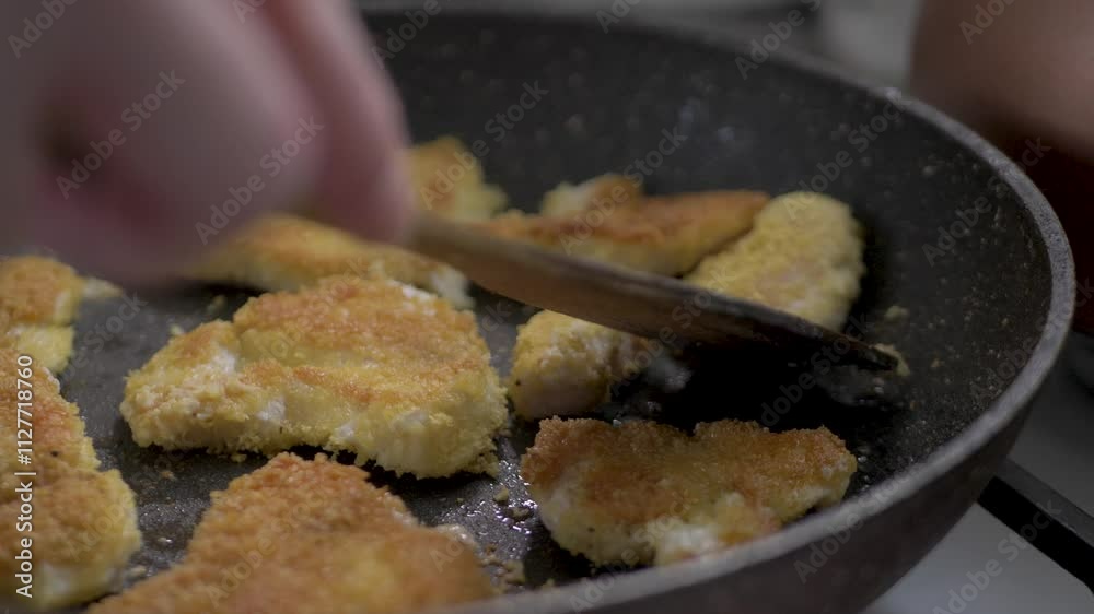 Pan of breaded chicken pieces is being cooked and turned golden brown with spatula. This process is part of making a delicious homemade meal. Cooking at home helps to maintain a balanced diet Pan of breaded chicken pieces is being cooked and turned golden brown with spatula. This process is part of making a delicious homemade meal. Cooking at home helps to maintain a balanced diet