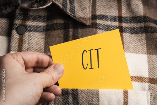 Yellow card with a handwritten inscription "CIT", a shaft in the hand, protruding from a brown plaid shirt (selective focus), translation: