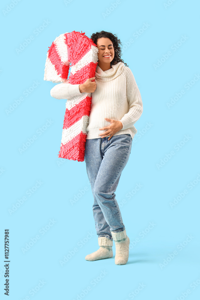 Pregnant African-American woman with candy cane pinata on blue background Pregnant African-American woman with candy cane pinata on blue background