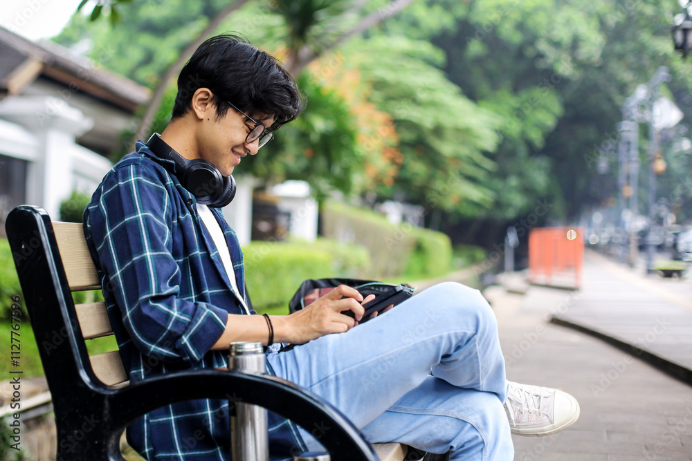 Obraz premium Young Man Using Digital Tablet on a Bench of The Urban Sidewalk