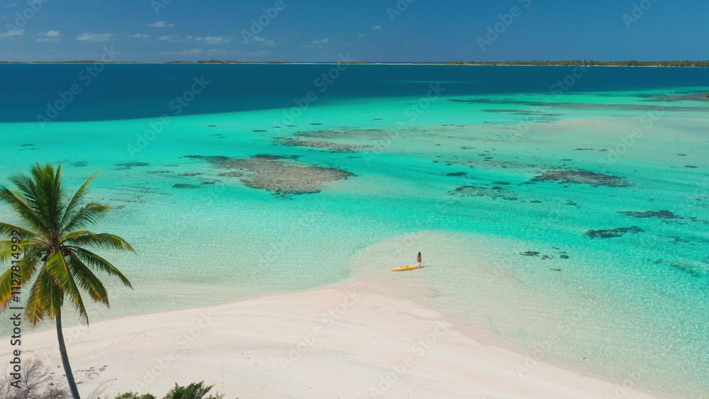 Fototapeta premium Aerial drone footage of a woman enjoying a sunny day on a tropical island with a yellow kayak, turquoise water, and a white sand beach