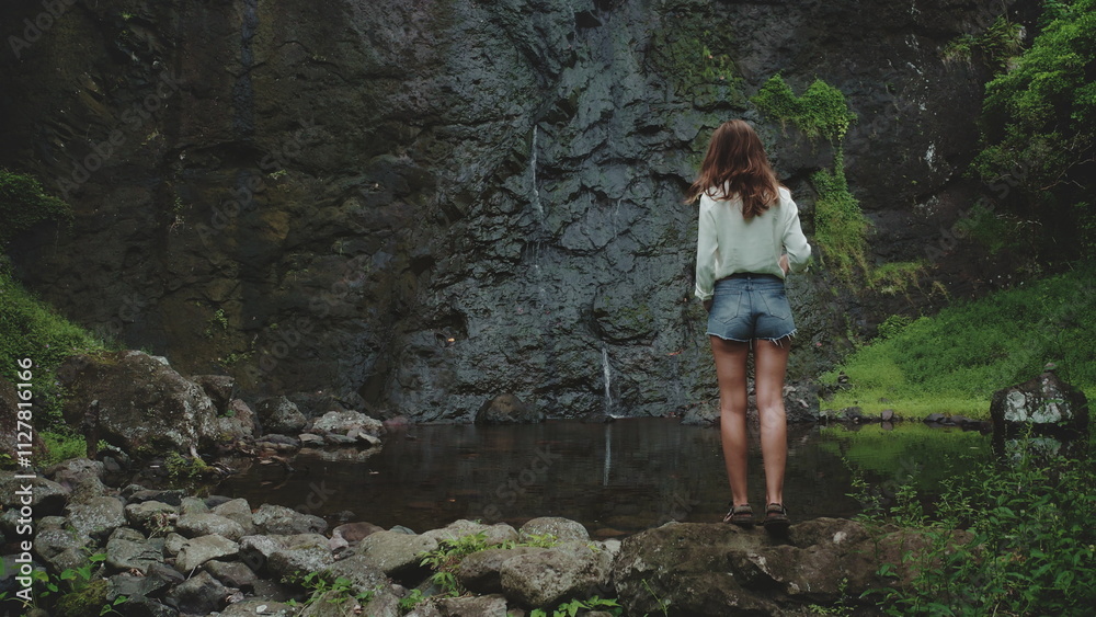 Woman tourist gazes at a waterfall from a cliff in a lush forest, embracing nature's beauty and tranquility Woman tourist gazes at a waterfall from a cliff in a lush forest, embracing nature's beauty and tranquility
