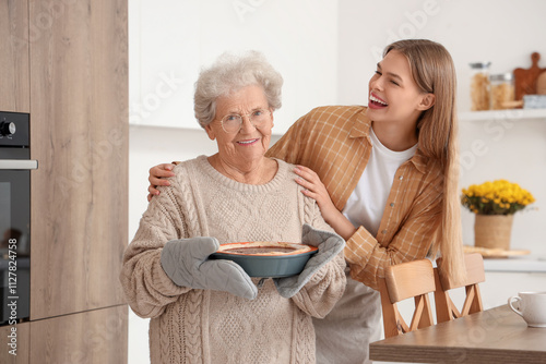 Young woman hugging her grandmother with tasty pie in kitchen
