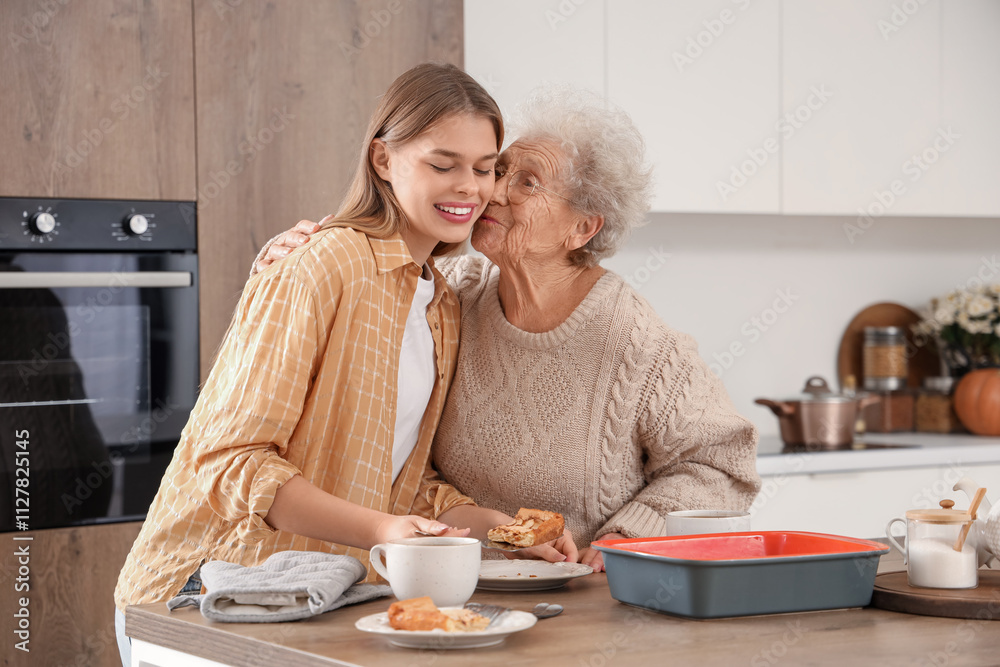 Senior woman kissing her granddaughter with tasty pie in kitchen