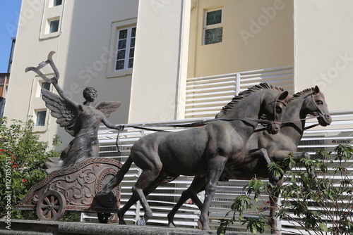 A bronze sculpture of the goddess Artemis on her chariot pulled by two horses stands in front of a modern apartment building photo