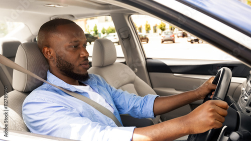 Confident Professional Driver. Side view profile portrait of young African American man sitting in a car on driver's seat. Focused black guy riding in the city, holding hands on steering wheel