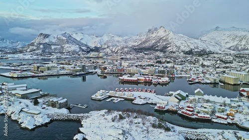 Snowy harbor town surrounded by dramatic mountains and calm waters in Svinøya, Lofoten Islands photo