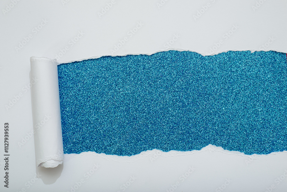 Obraz premium Torn white paper revealing a blue glitter background.