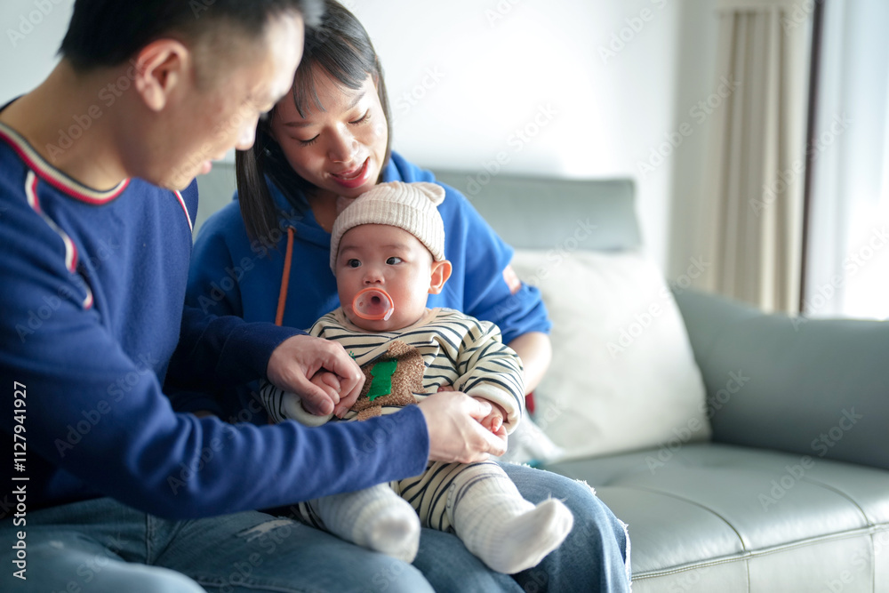 Fototapeta premium A 6-month-old boy spends time on a couch with his mother and father from a Chinese family on a cold winter day in an apartment building in the Pudong New Area of ​​Shanghai, China.