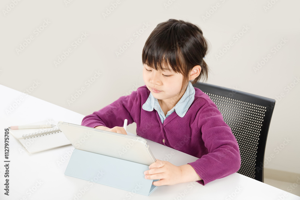 集中してタブレット操作しながら勉強している小学生の女の子