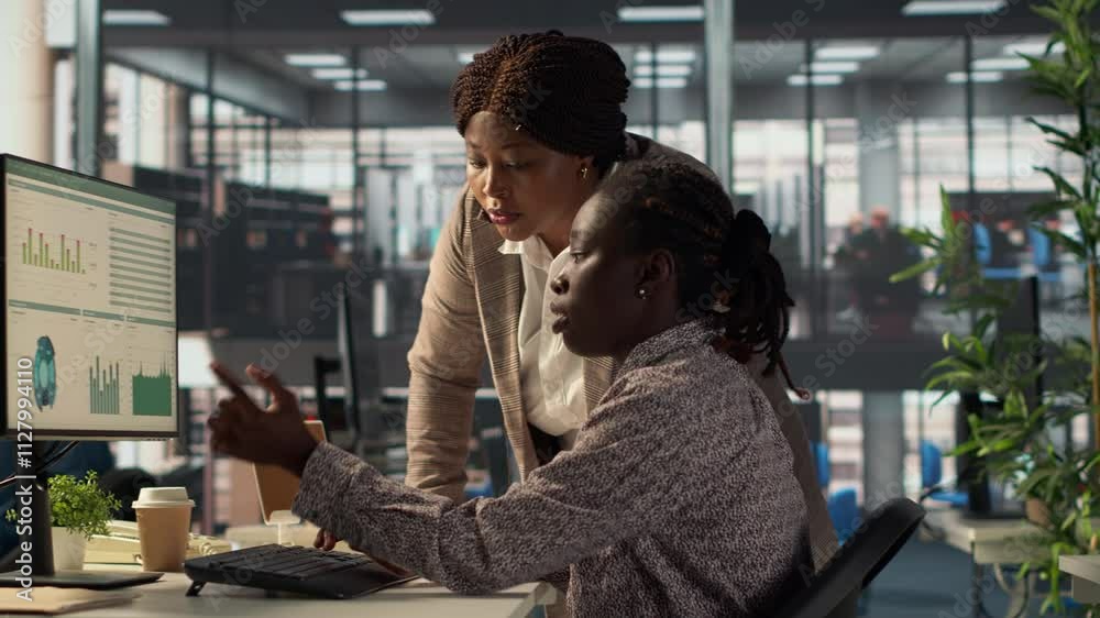 Female employee and manager gathered around a workstation discussing objectives and strategizing solutions to solve administrative tasks faster. Aligning business goals and milestones. Camera A.