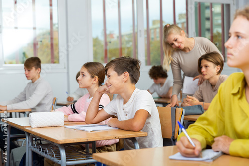 Teen boys and girls sitting at desk in classroom full of pupils during lesson