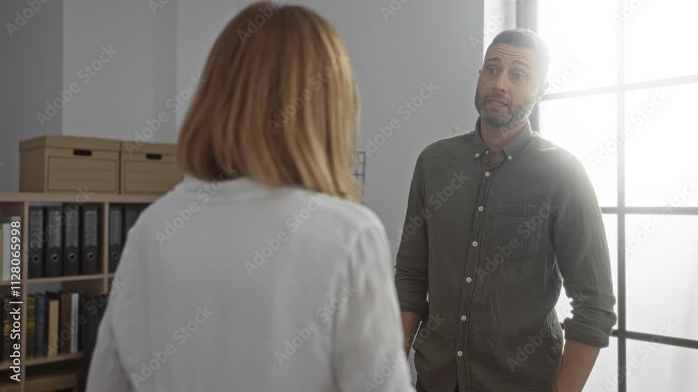 Man and woman discussing business in a modern office environment with shelves and boxes in the background Man and woman discussing business in a modern office environment with shelves and boxes in the background