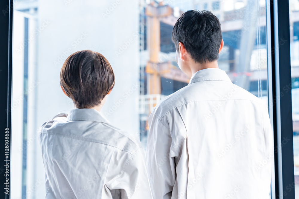 Obraz premium 工事現場をバックに窓の外を見つめる男女
