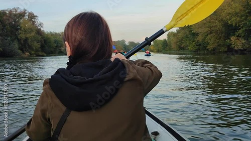 Woman sitting in an inflatable boat and rowing an oar, floating on the river with other people in boats on an autumn day. Many trees on banks. Kayaking tourism travel sport entertainment rest relax photo