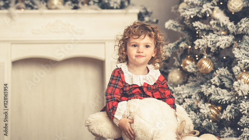 Kleines hübsches Mädchen mit Weihnachtskleidung und Teddybär in Weihnachtskulisse und Kamin Var. 4