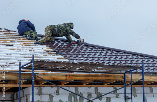 Two men are working on a roof, one of them is wearing a camouflage jacket photo