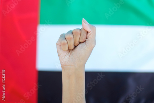 Close Up Of Raised Hand Clenching Fist Against UAE National Flag Background photo