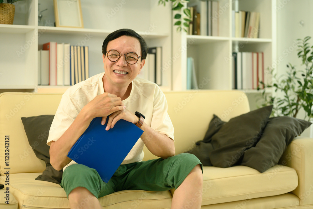 Cheerful middle aged man wearing glasses and casual clothed sitting on sofa in a cozy living room Cheerful middle aged man wearing glasses and casual clothed sitting on sofa in a cozy living room