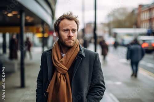 Portrait of a handsome young man with a beard wearing a coat and a scarf in the city.