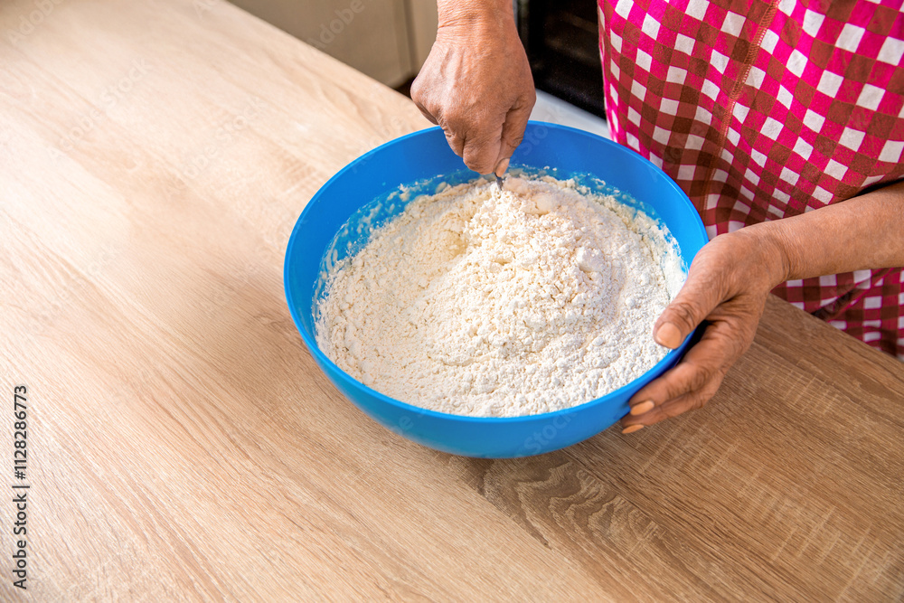 Woman stirs around spoon in bowl flour. Woman kneading dough by hand yeast dough. Woman hands and dough in a blue metal bowl. Female chef preparing dough on kitchen table