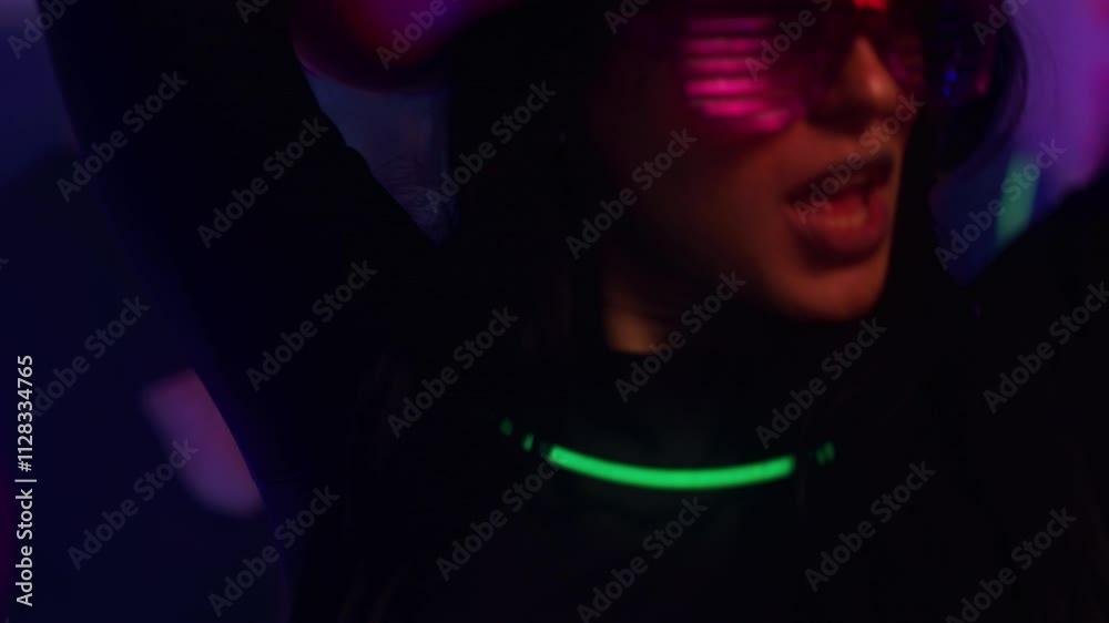 A cool hip girl wearing a pink cowboy hat and cool sunglasses dances and looks at the camera at a party.