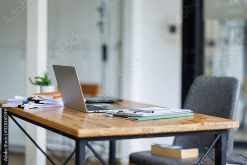 Laptop Computer, notebook, and eyeglasses sitting on a desk in a large open plan office space after working hours 