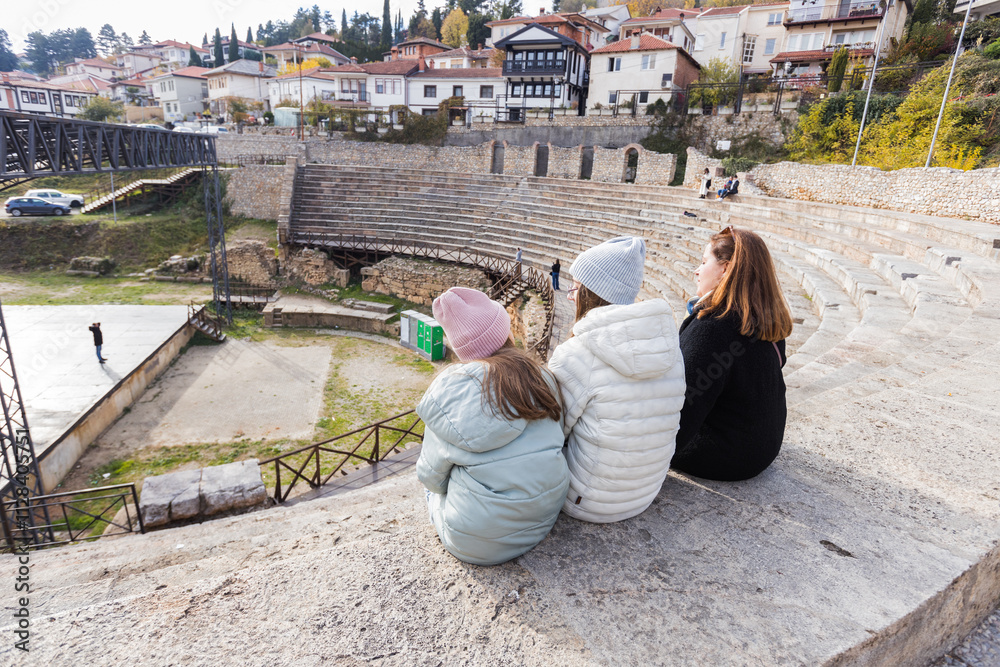 Fototapeta premium Family sitting on stone steps at Ancient Theatre Of Ohrid, North Macedonia.