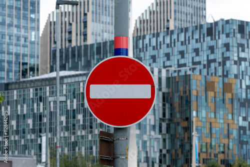 A vibrant no entry road sign stands prominently in front of impressive contemporary buildings, emphasizing the intersection of urban regulations and modern architecture.