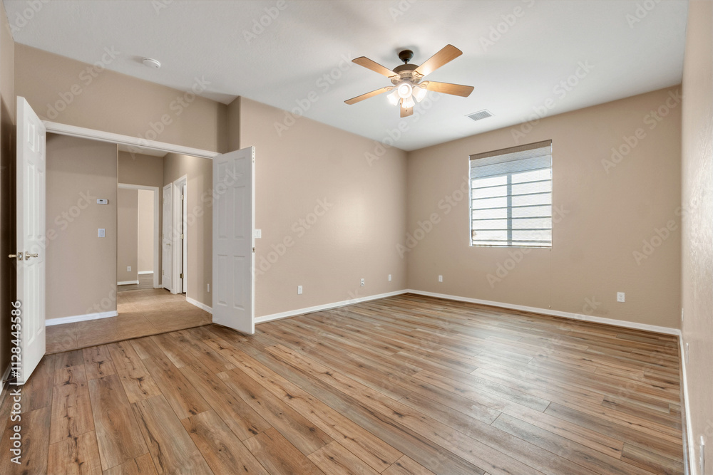 Spacious empty room with wooden flooring and ceiling fan in a residential setting Spacious empty room with wooden flooring and ceiling fan in a residential setting