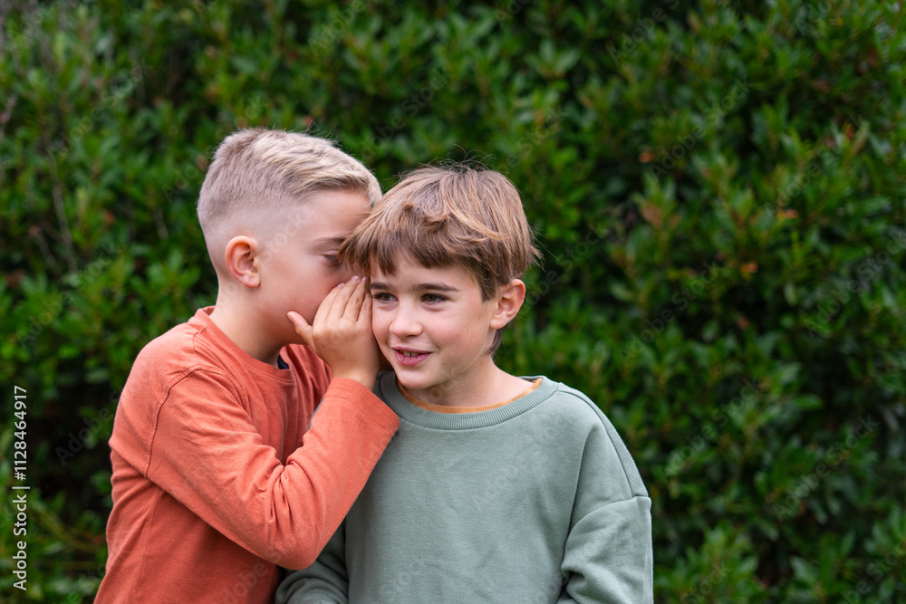 Boy whispering a secret to his friend in a green park Boy whispering a secret to his friend in a green park