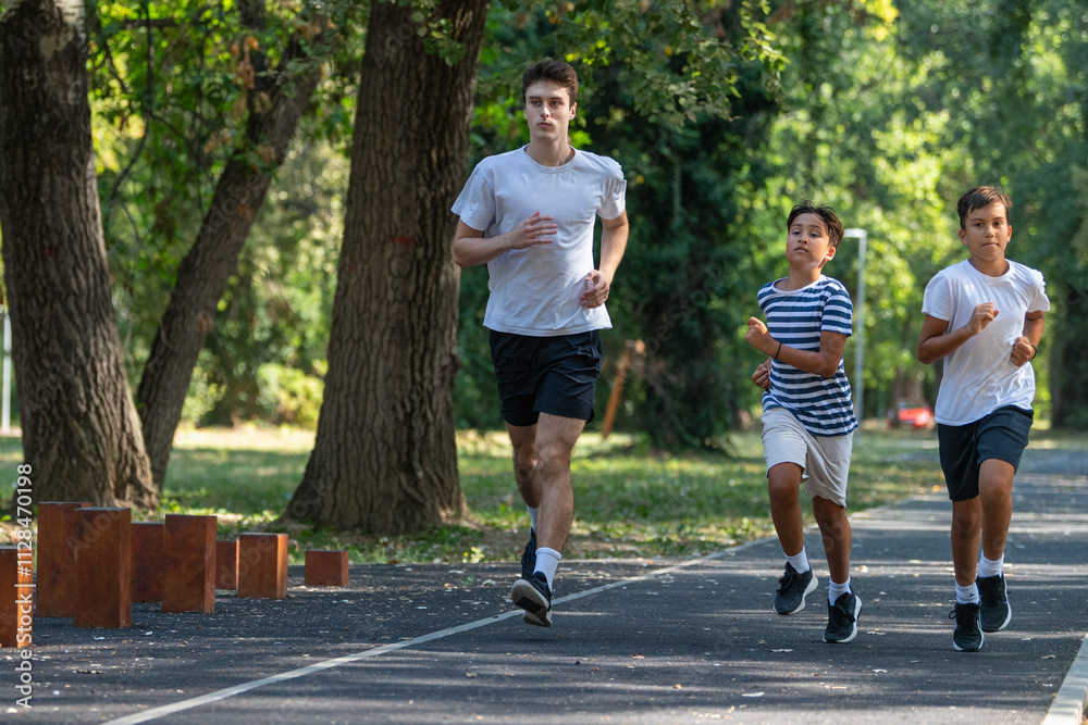 Trainer runs alongside two boys in a sunny park, focusing on improving their endurance and physical fitness. The boys are energized, learning proper running techniques while enjoying outdoor exercise Trainer runs alongside two boys in a sunny park, focusing on improving their endurance and physical fitness. The boys are energized, learning proper running techniques while enjoying outdoor exercise