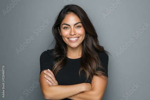 Smiling hispanic young female in casual black shirt with arms crossed against gray background