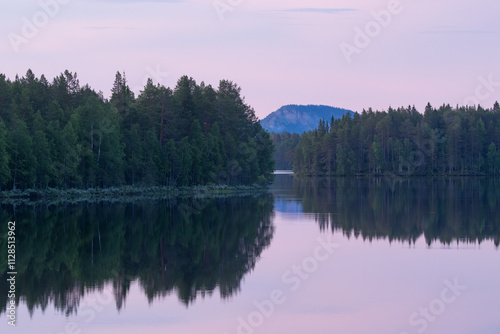 A Northern landscape with a calm lake, forest on banks and a large hill in distance on a summer night near Kuusamo, Finland