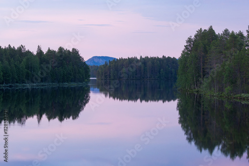 A Northern landscape with a calm lake, forest on banks and a large hill in distance on a summer night near Kuusamo, Finland