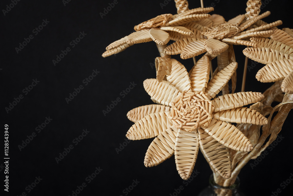 A bouquet of flowers made of straw in a glass vase on a black background. Straw weaving A bouquet of flowers made of straw in a glass vase on a black background. Straw weaving