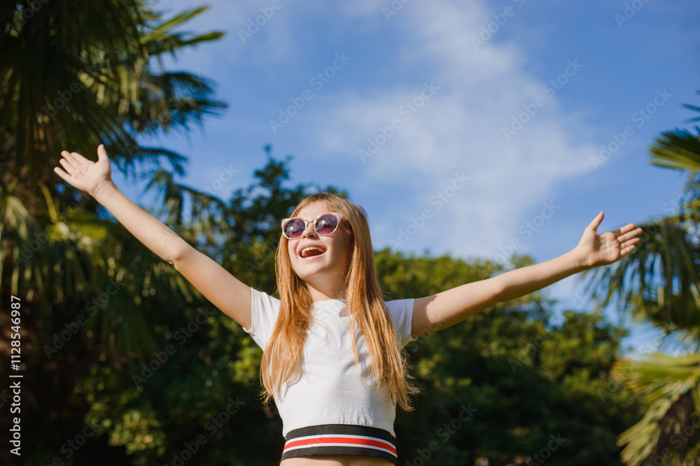 A teenage girl with long hair against the sky in a park wearing a hat and sunglasses