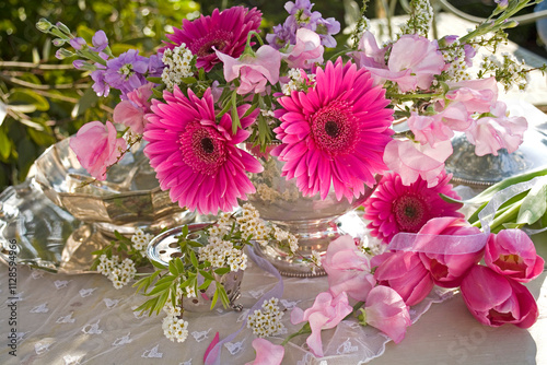 Crimson gerbera flowers still life in a silver bowl with sweet peas on a table outdoors in a garden photo